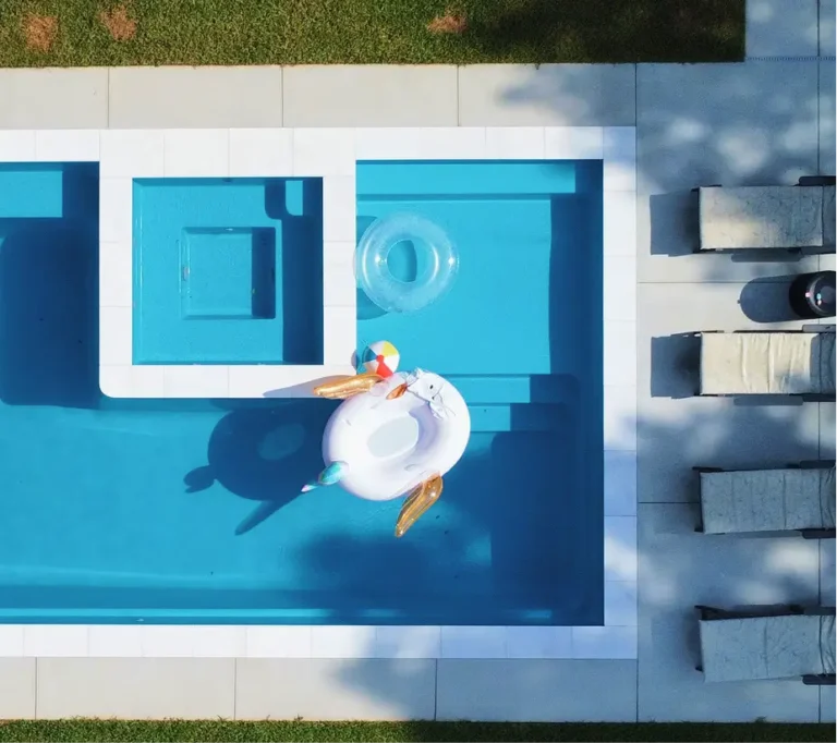 Aerial view of a modern swimming pool remodel by Legacy Pools featuring a built-in spa, tanning ledge, and vibrant blue water.