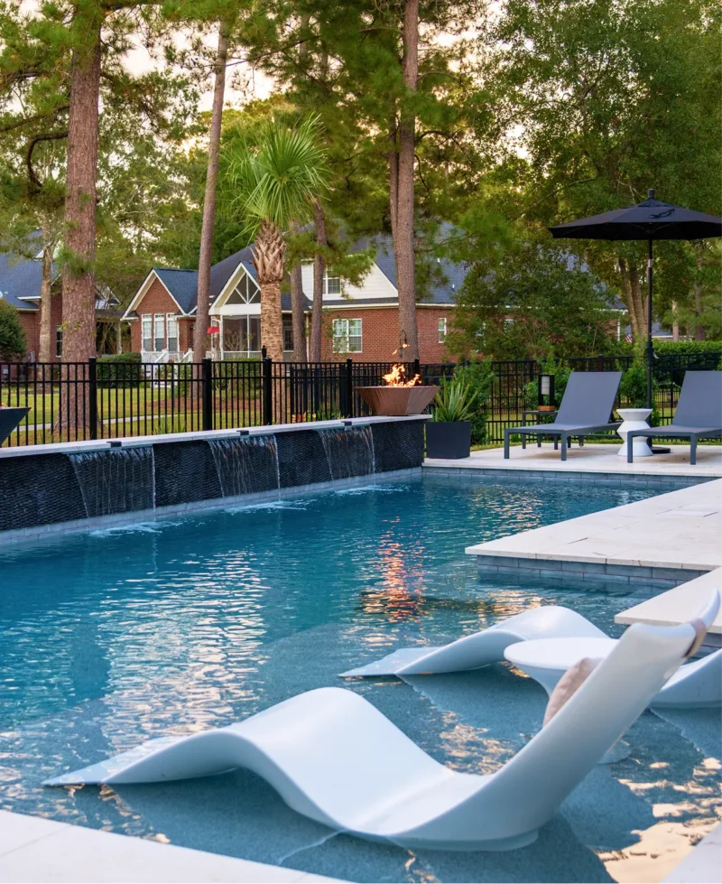 Modern patio featuring a luxury pool with submerged lounge chairs, tiered fountains, and classic brick architecture in South Carolina