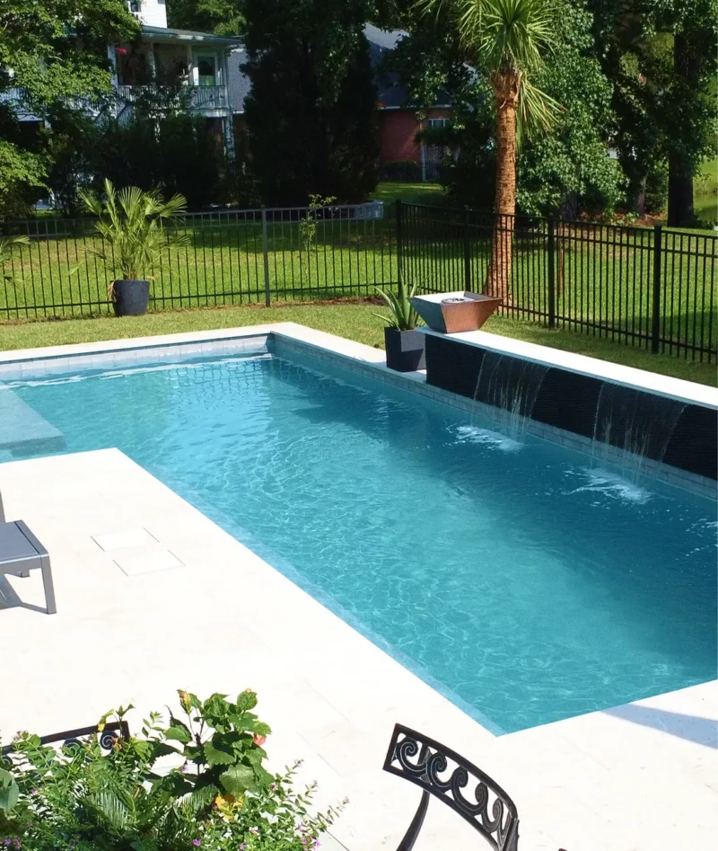 Modern pool remodel by Legacy Pools featuring a custom black tile waterfall wall and white stone patio.