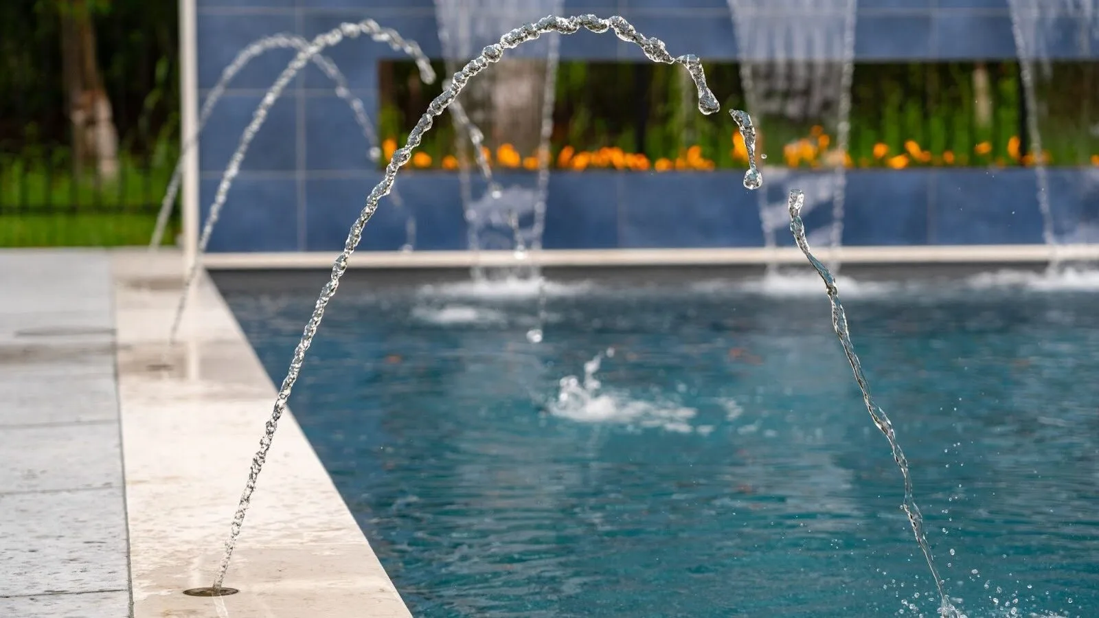 Luxury pool water features with arcing deck jets, finished tile, and clear blue water.
