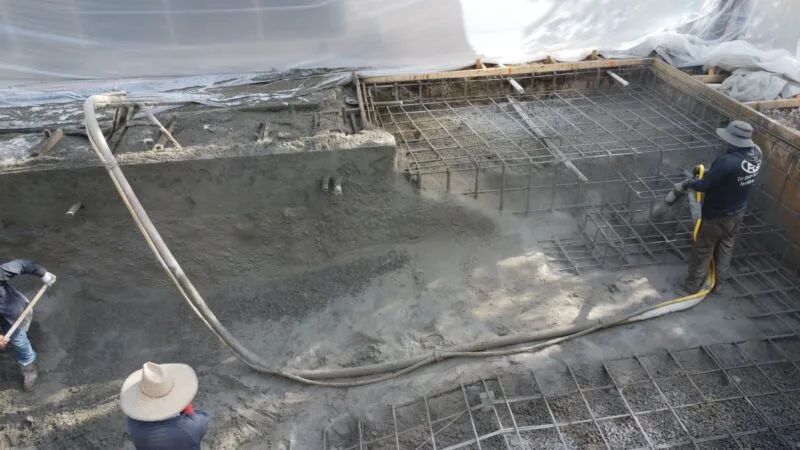 A group of people spraying gunite concrete on a steel rebar pool shell frame
