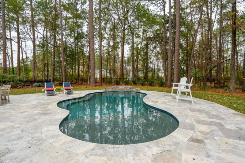 A backyard gunite pool with chairs and tiled pool decking