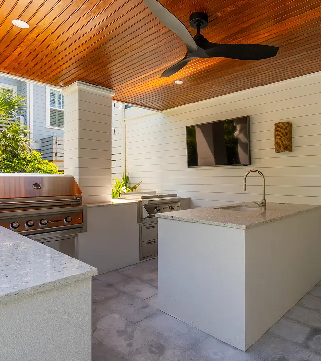 Outdoor kitchen with grill, TV, and ceiling fan under a wood-paneled ceiling.