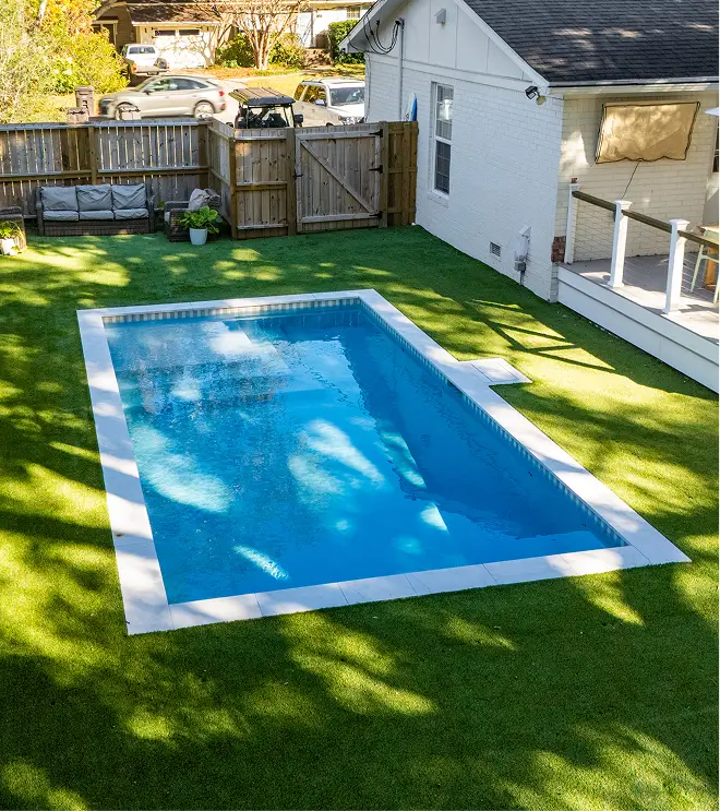Small rectangular pool in a private backyard with artificial turf.